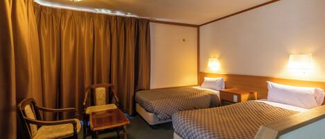 A hotel room with two beds, a desk, two chairs, and a nightstand with lamps.