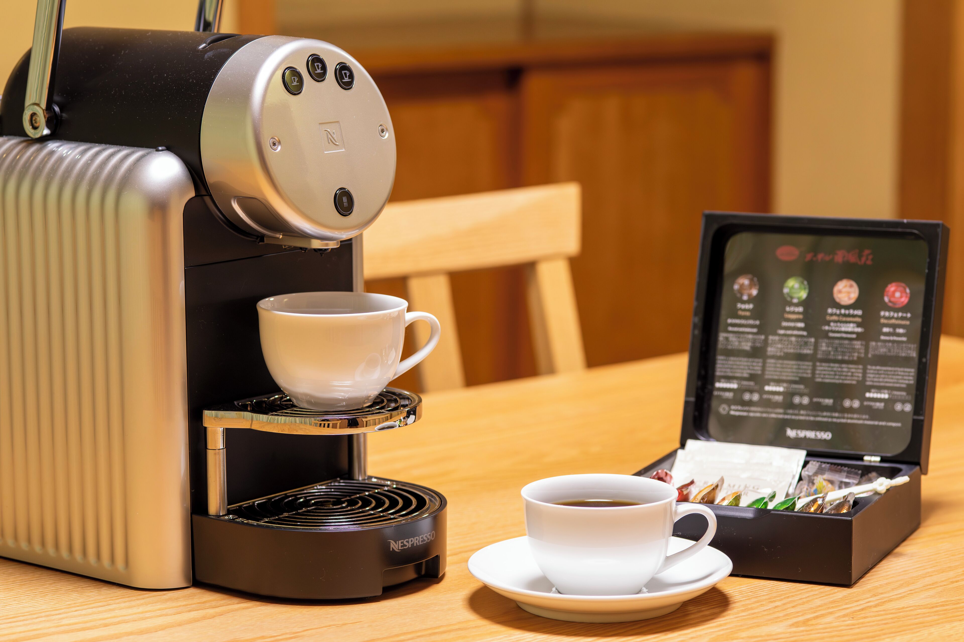 A Nespresso coffee machine with a cup of coffee and a box of coffee capsules on a wooden table.