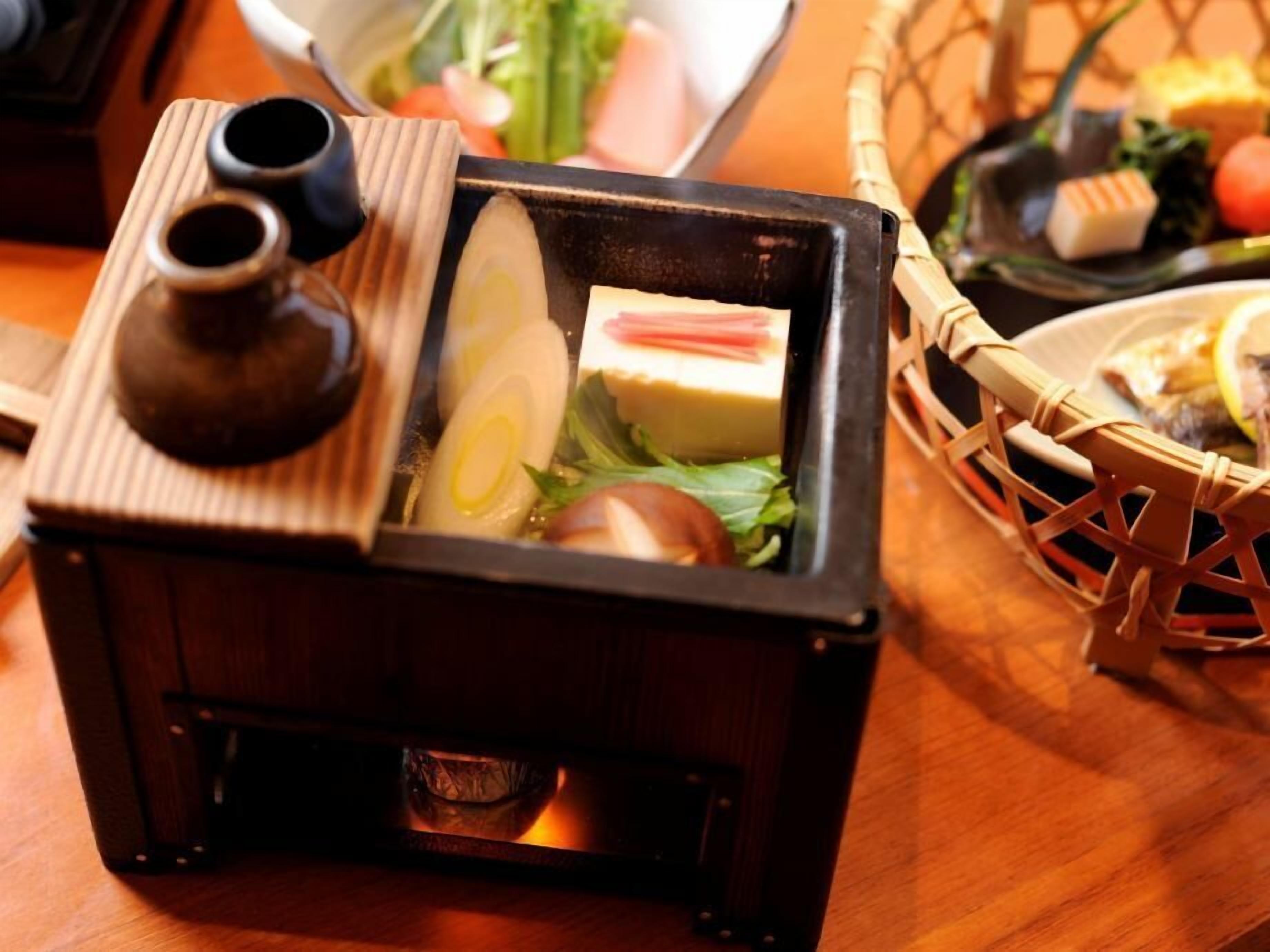 A traditional Japanese hot pot setup with a wooden table, a woven basket, and various vegetables and tofu.