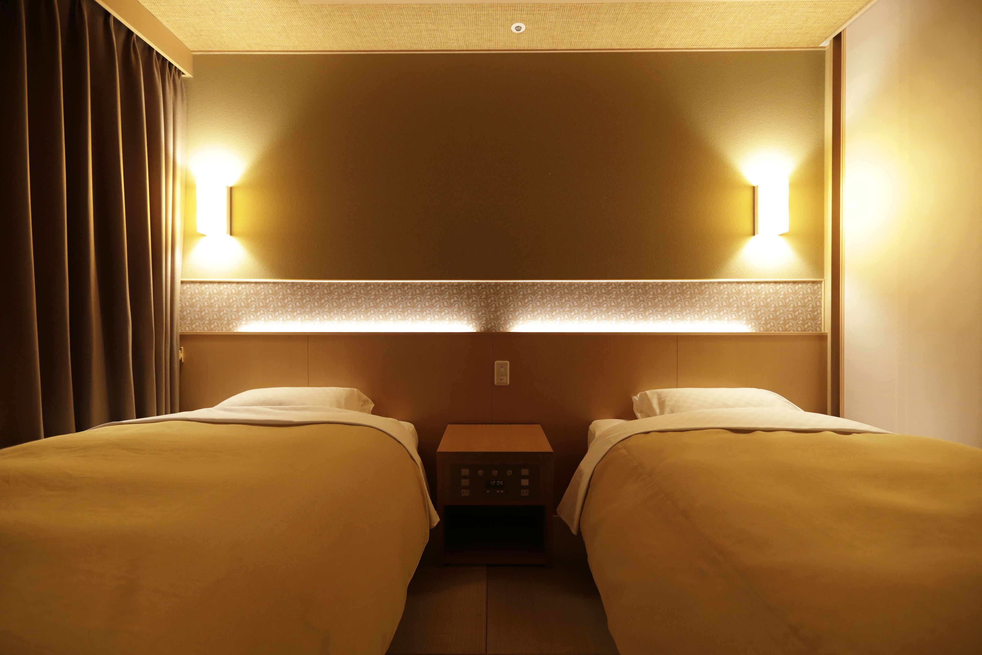 A hotel room with two beds, a nightstand, and wall-mounted lights.