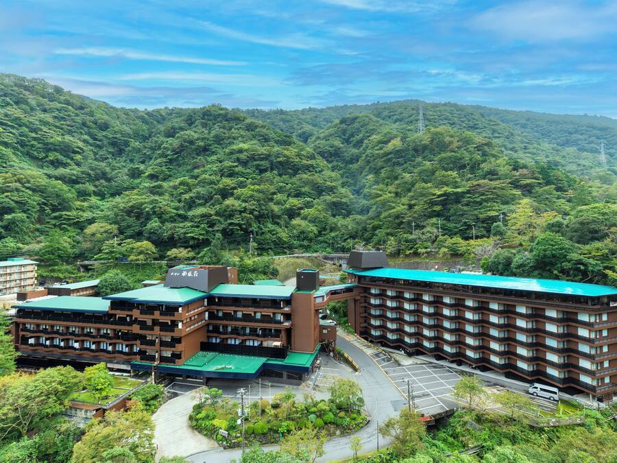 Un hotel de varios pisos con techo verde, rodeado de abundante vegetación y colinas.