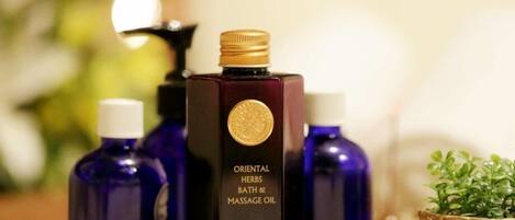 A bottle of Oriental Herbs Bath & Massage Oil with a gold cap, surrounded by other bottles.
