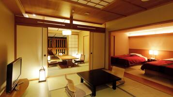 A traditional Japanese-style hotel room with tatami flooring, a low table, a television, and two beds with red bedding.