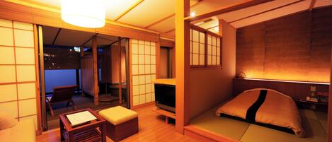 A traditional Japanese-style room with tatami flooring, a low wooden bed, a television, and sliding shoji doors.