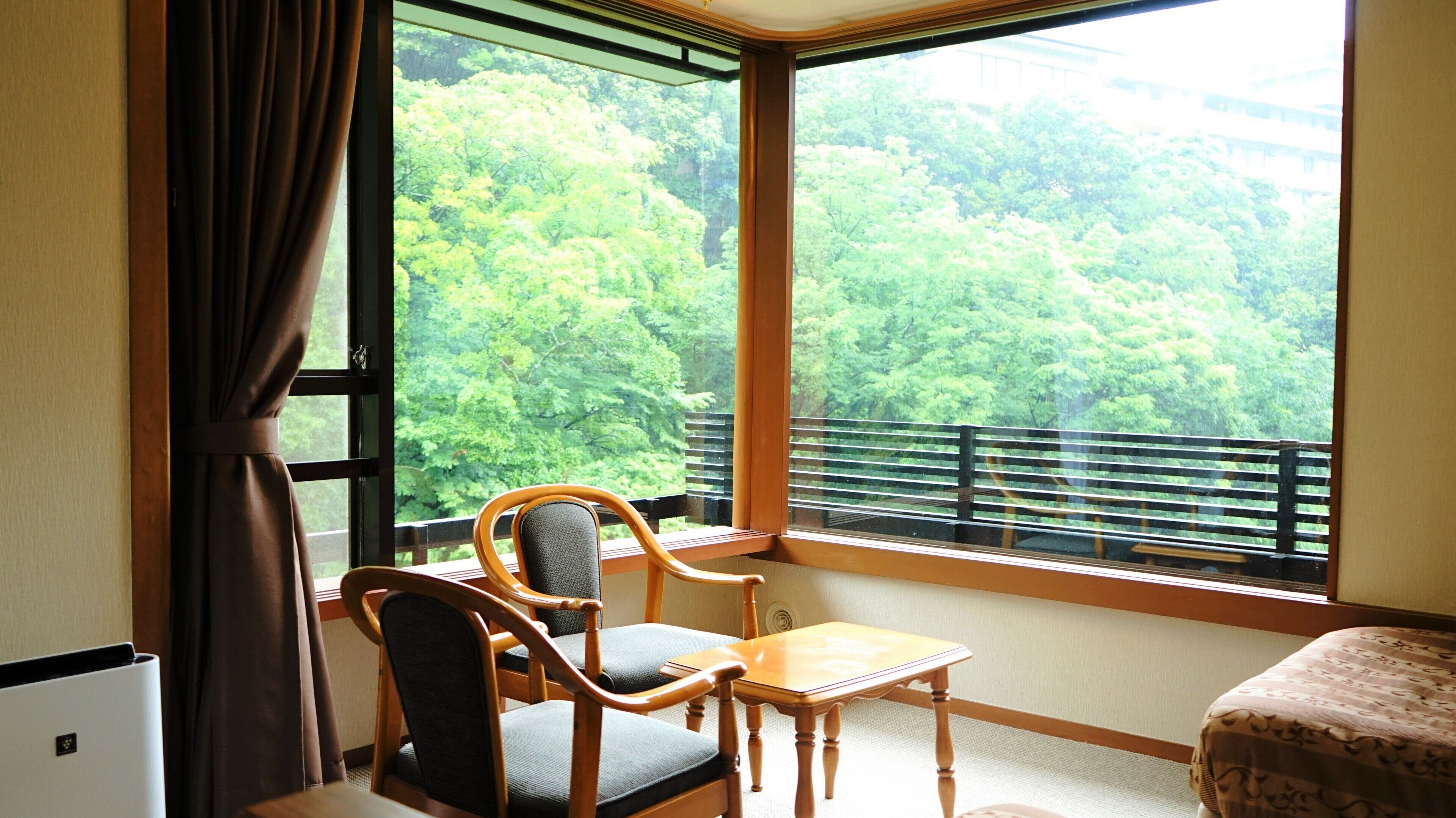 A room with a large window, a chair, a small table, and a bed.