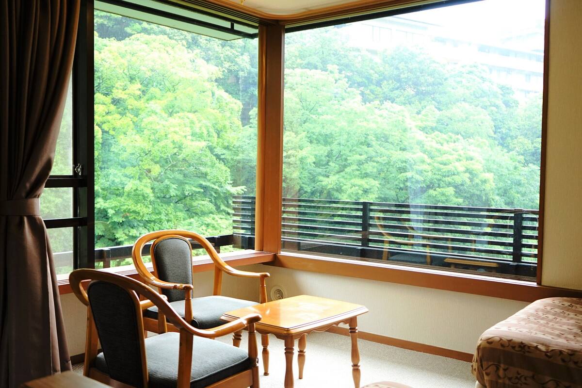 A room with a large window, a chair, a small table, and a bed.
