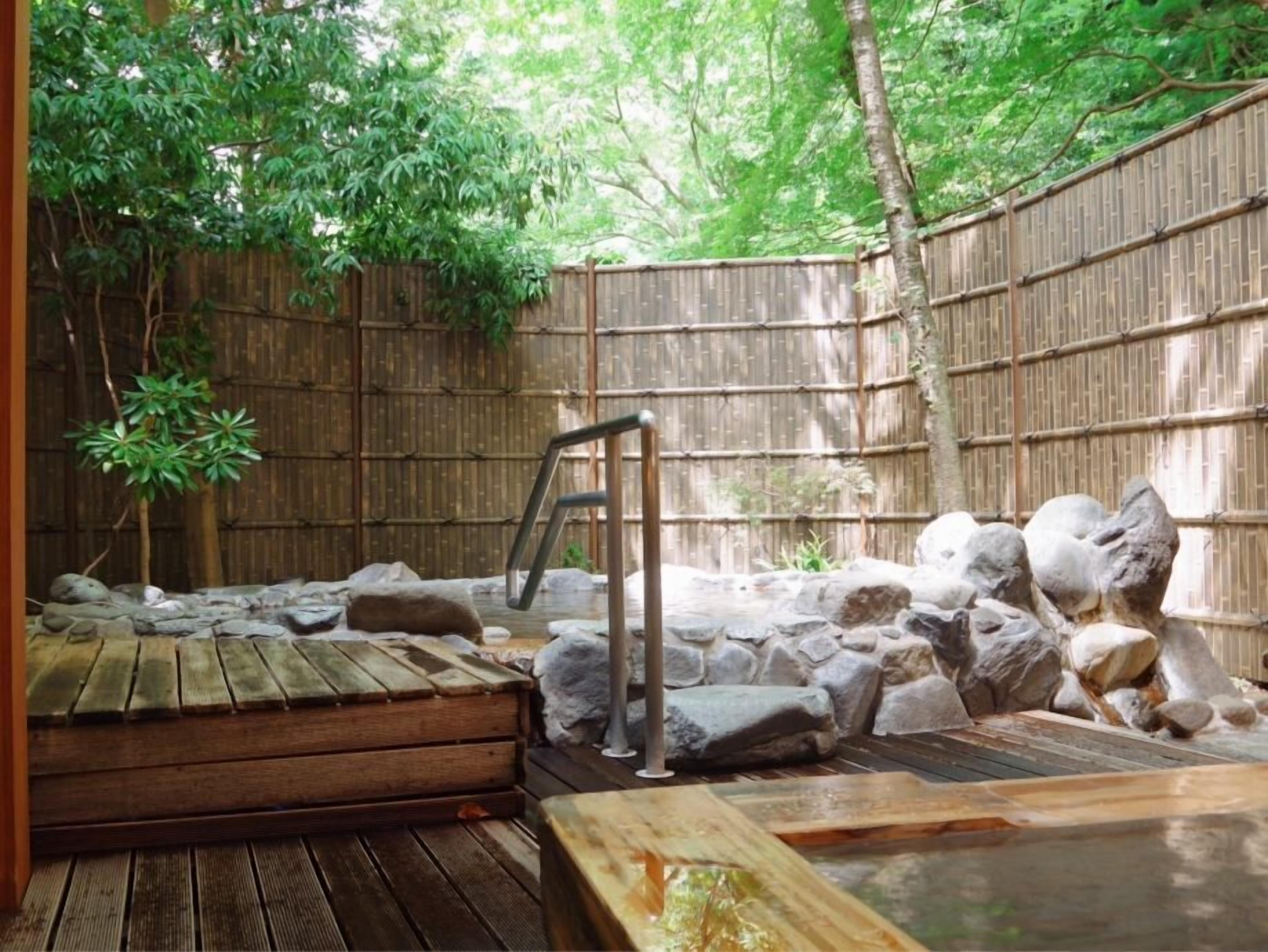 A hot spring area with a wooden deck, stone seating, and a bamboo fence.