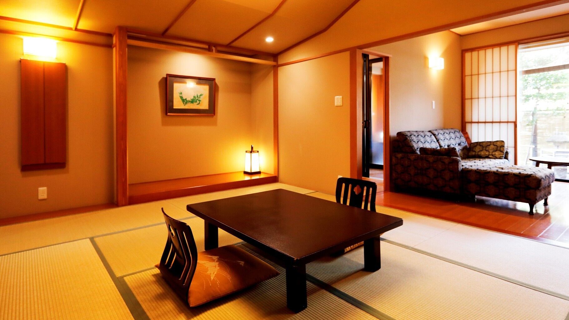 A traditional Japanese room with tatami flooring, a low table with chairs, a sofa, and a picture on the wall.