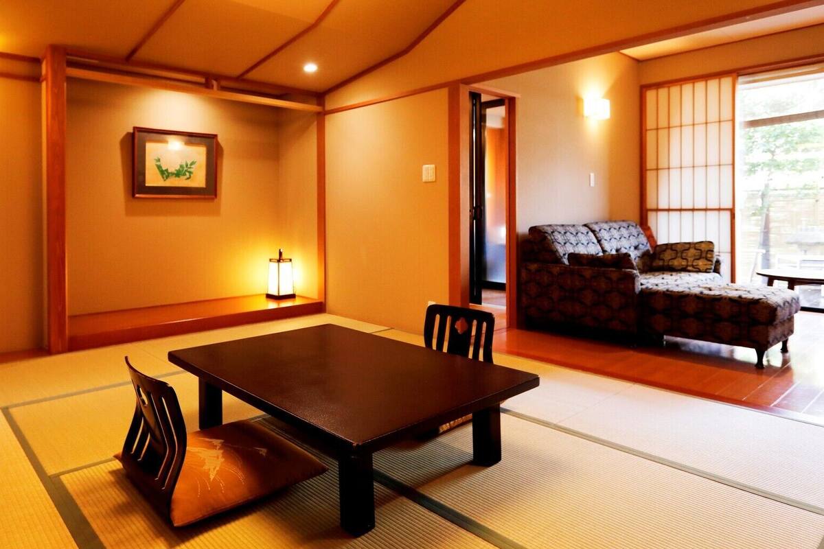 A traditional Japanese room with tatami flooring, a low table with chairs, a sofa, and a picture on the wall.