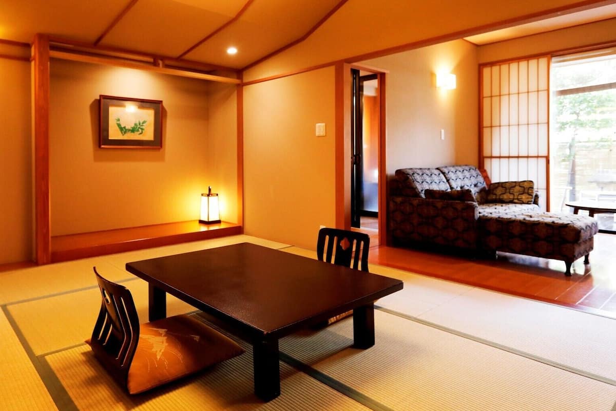 A traditional Japanese room with tatami flooring, a low table with chairs, a sofa, and a picture on the wall.