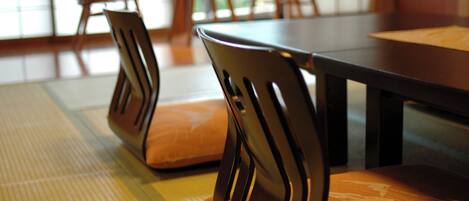 A dining area with wooden chairs and a table, featuring a woven mat on the floor.