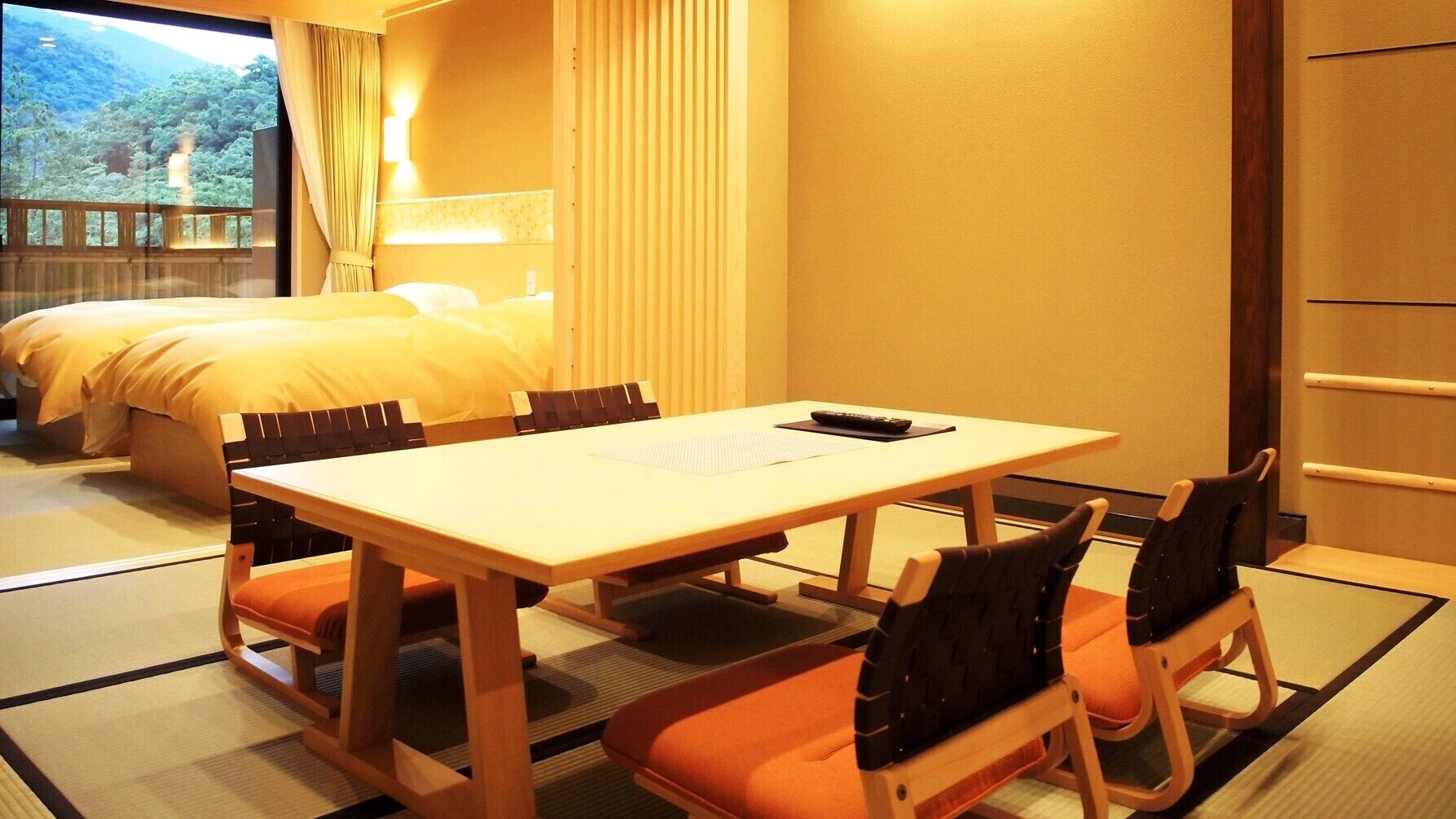 A hotel room with a bed, a dining table with chairs, and a view of a forest.
