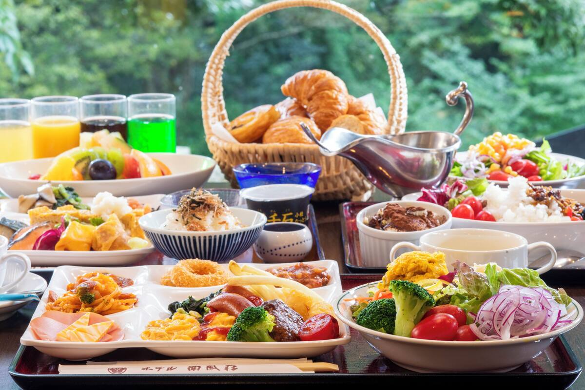A variety of dishes and drinks on a table with a view of greenery in the background.