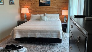 Un dormitorio con una cama, dos mesitas de noche con lámparas, un cabecero de madera, un cuadro y un aparador.