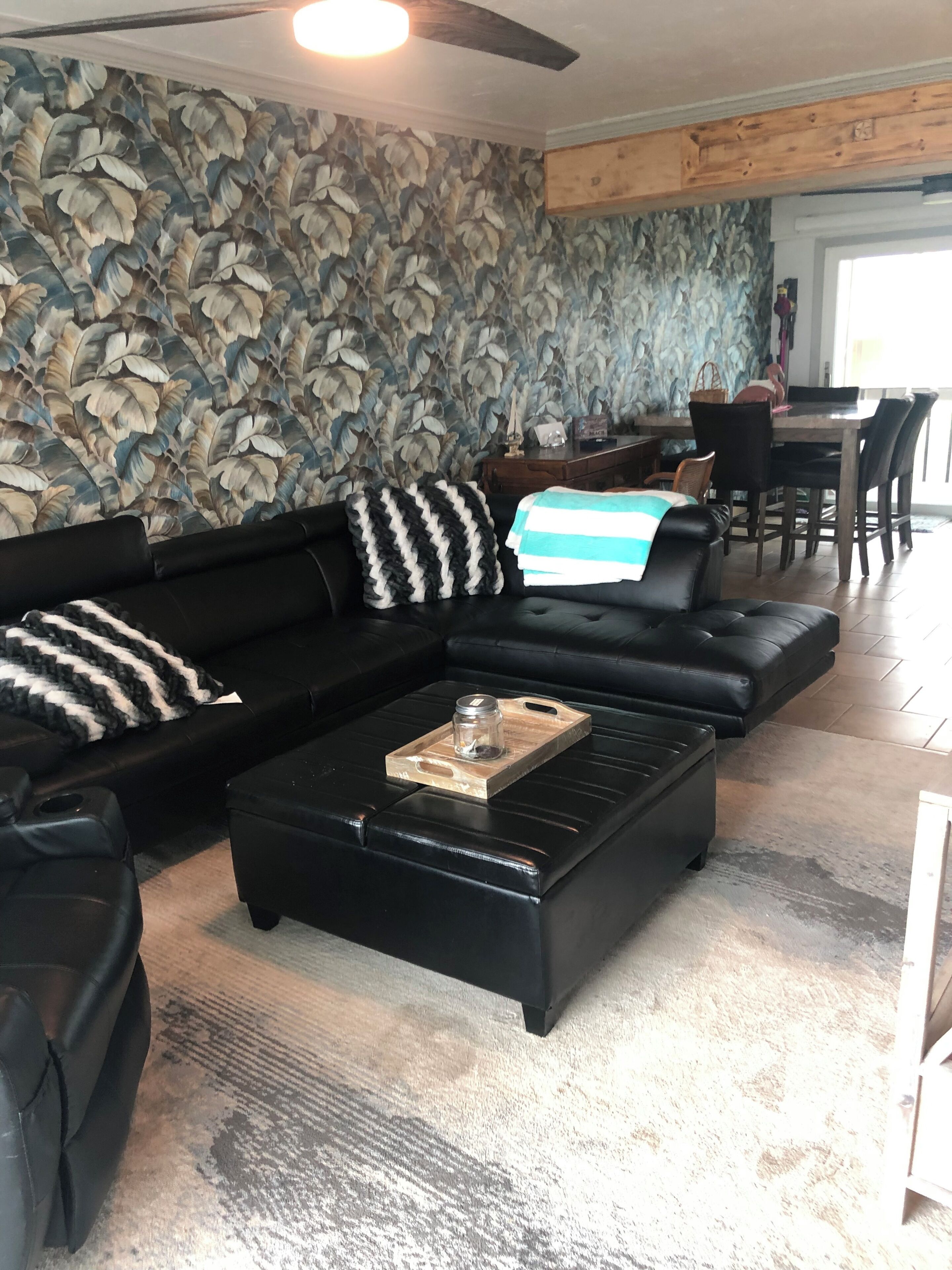 Un salon moderne avec un canapé en cuir noir, une table basse surmontée d’un bocal en verre et un mur orné d’un motif.