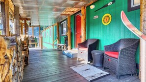 A covered porch with wicker furniture, a wooden deck, and a green wall with a clock. - Rainier Bunkhouse & Bar-Cade- HotTub,MtnView,2 blks to Packwood Brewing! Pets ok (Packwood)