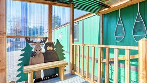 A wooden deck with a bench, a green wall with a window, and a decorative wall hanging. - Rainier Bunkhouse & Bar-Cade- HotTub,MtnView,2 blks to Packwood Brewing! Pets ok (Packwood)