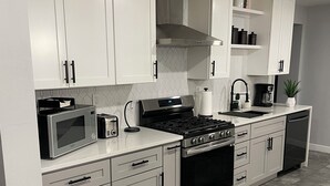 Een moderne keuken met witte kasten, een roestvrijstalen fornuis, een magnetron en een vaatwasser.