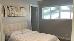 Een slaapkamer met een groot bed, een plafondventilator, een raam met jaloezieën en een deur.