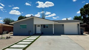 Een gelijkvloers huis met een garage, een voortuin met een betonnen pad en een helderblauwe lucht.