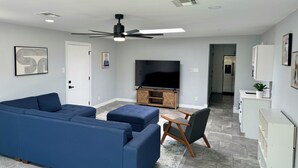 Een moderne woonkamer met een blauwe bank, een houten salontafel en een televisie op een houten dressoir.