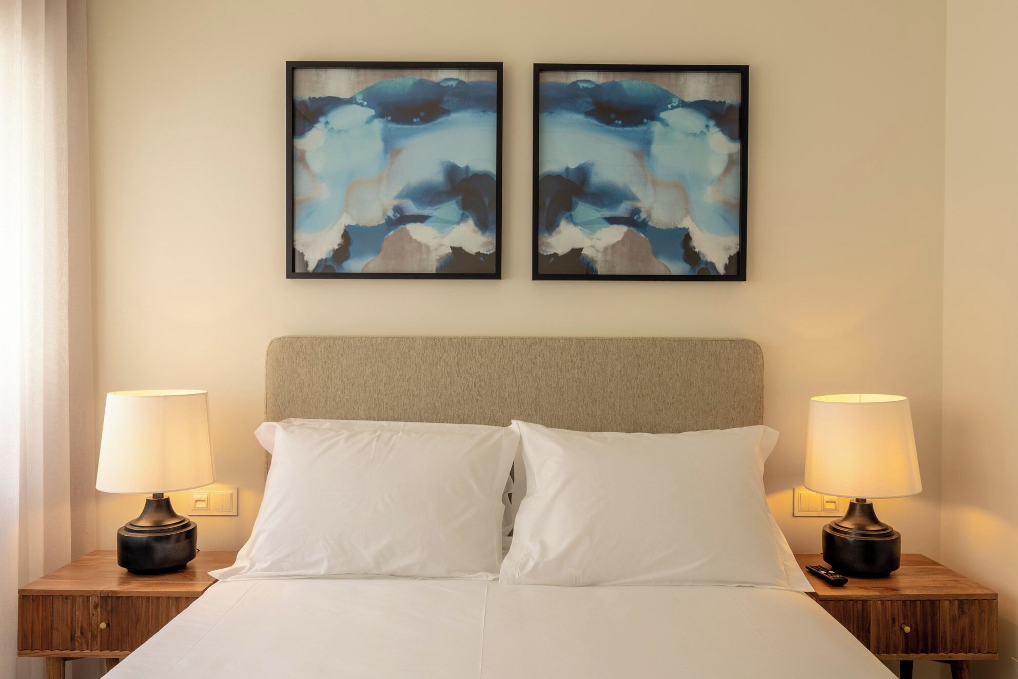 A hotel room with a bed, two nightstands, two lamps, and two framed abstract paintings on the wall.