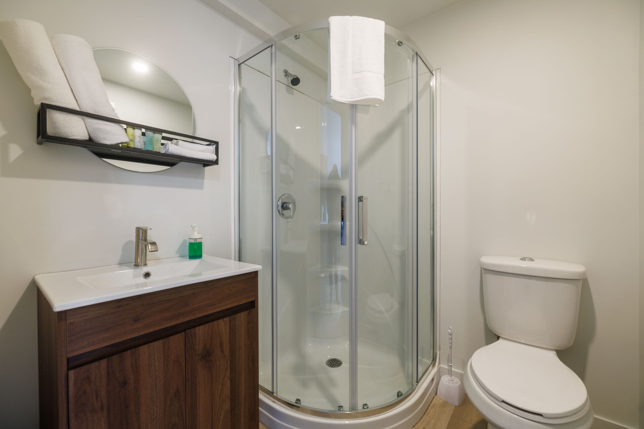 Ein Badezimmer mit einer Duschkabine aus Glas, einem weißen Waschbecken mit Holzschrank und einer Toilette.
