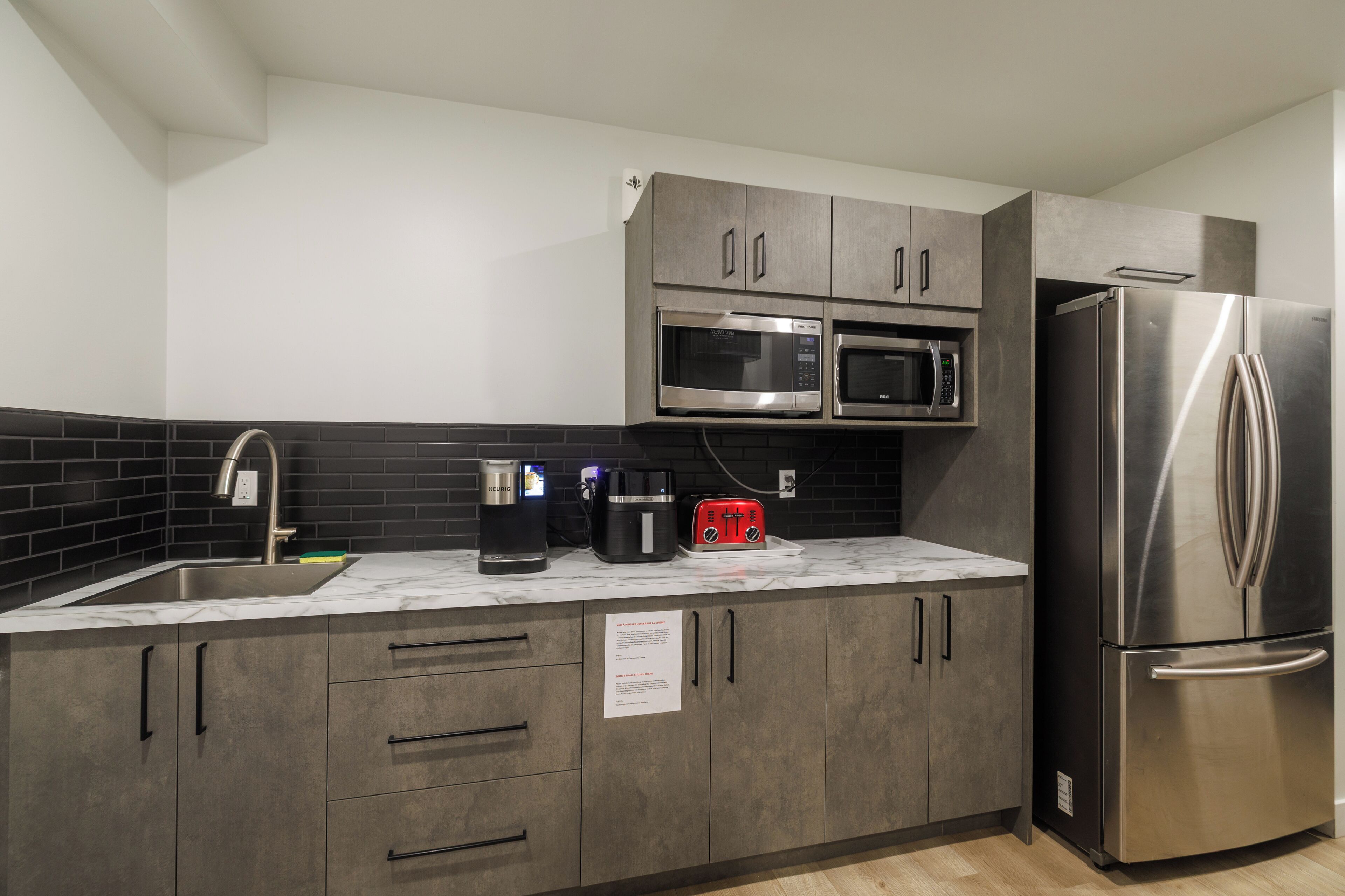 A modern kitchen with grey cabinets, a stainless steel refrigerator, a microwave, and a coffee maker.
