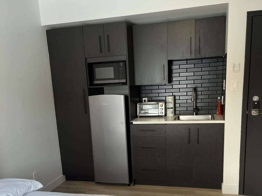 Habitació d'hotel petita amb llit, cuineta i armari fosc.
