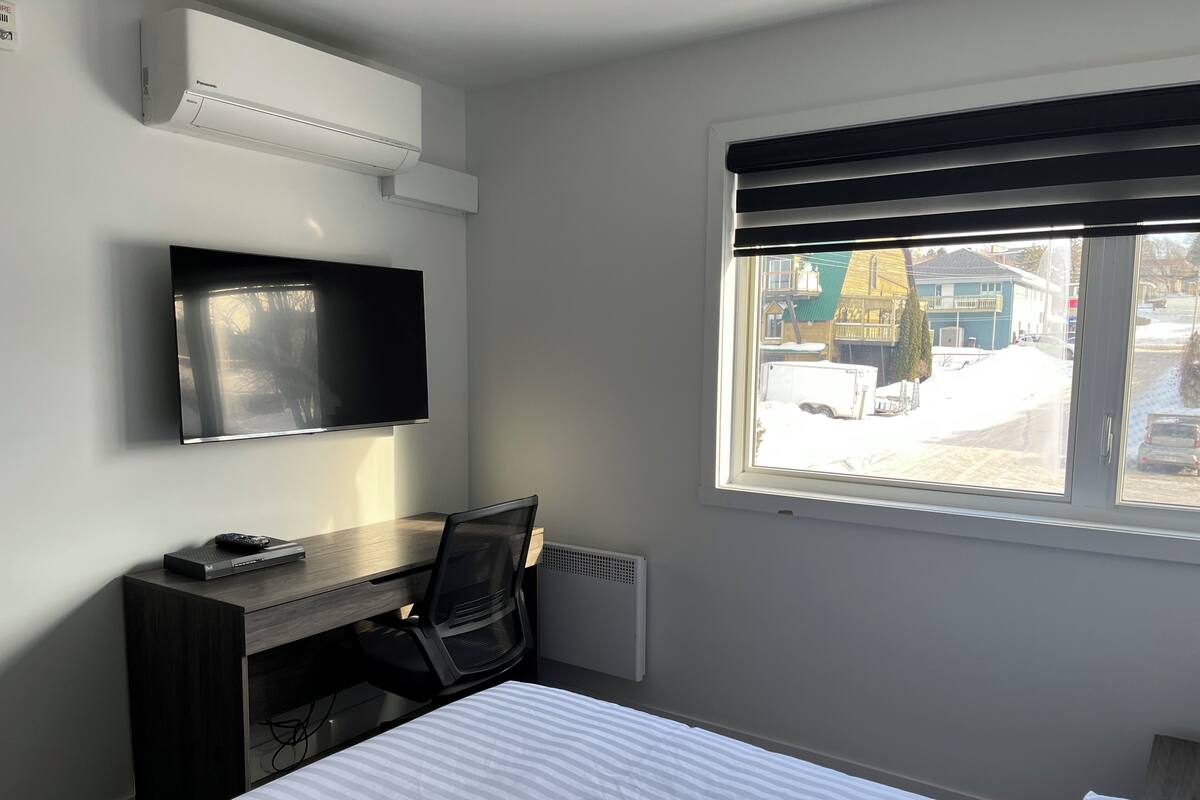 A hotel room with a bed, a desk with a chair, a television, and a window with a view of the outside.