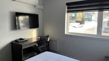 A hotel room with a bed, a desk with a chair, a television, and a window with a view of the outside.