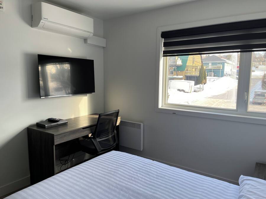 A hotel room with a bed, a desk with a chair, a television, and a window with a view of the outside.