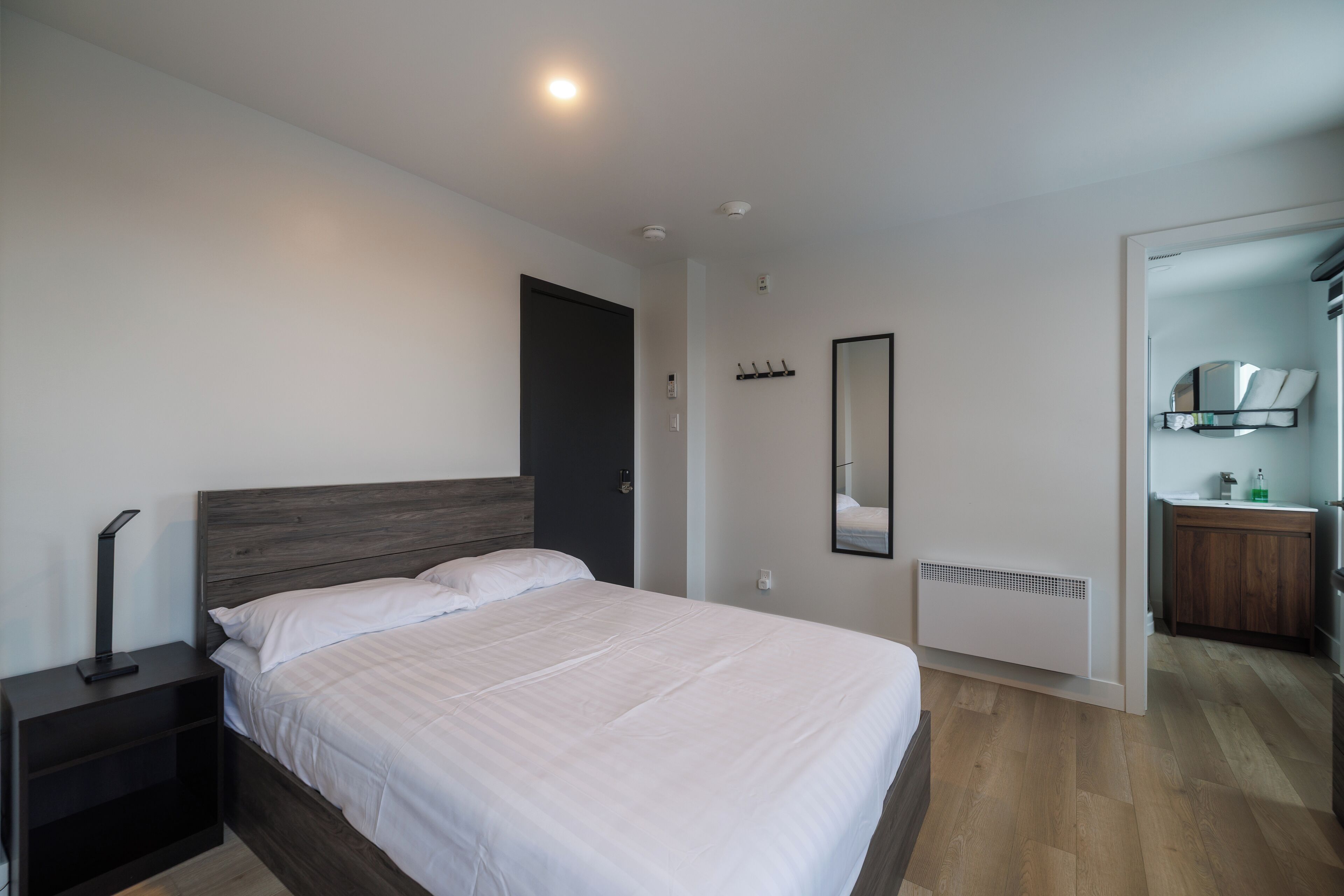 A modern bedroom with a bed, bedside table, and a mirror.