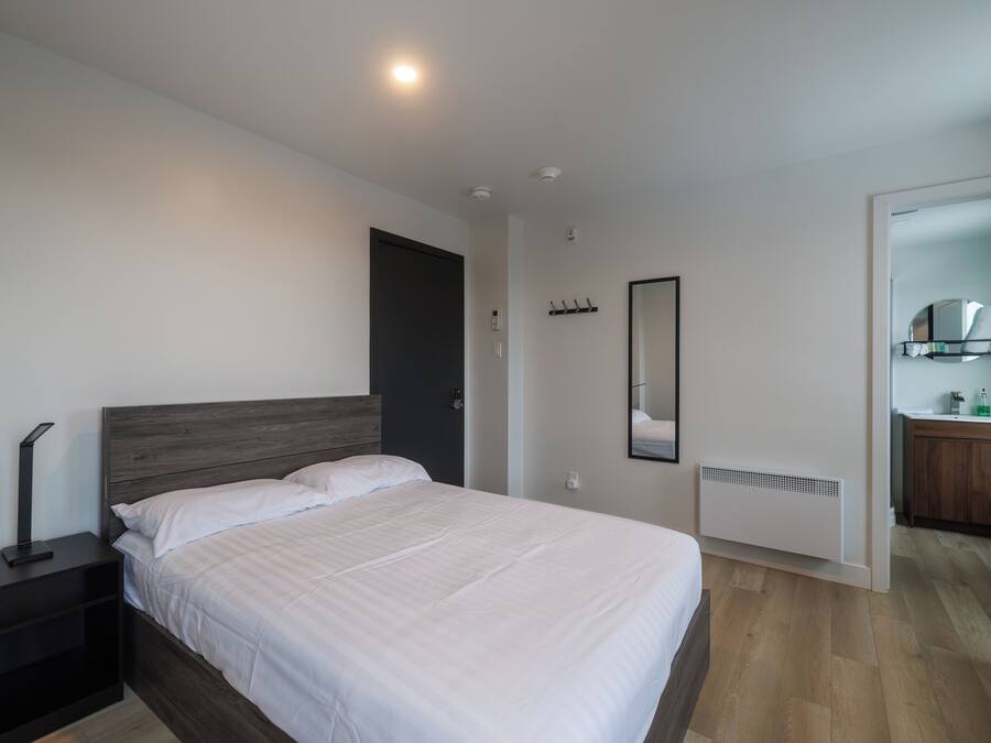 A modern bedroom with a bed, bedside table, and a mirror.