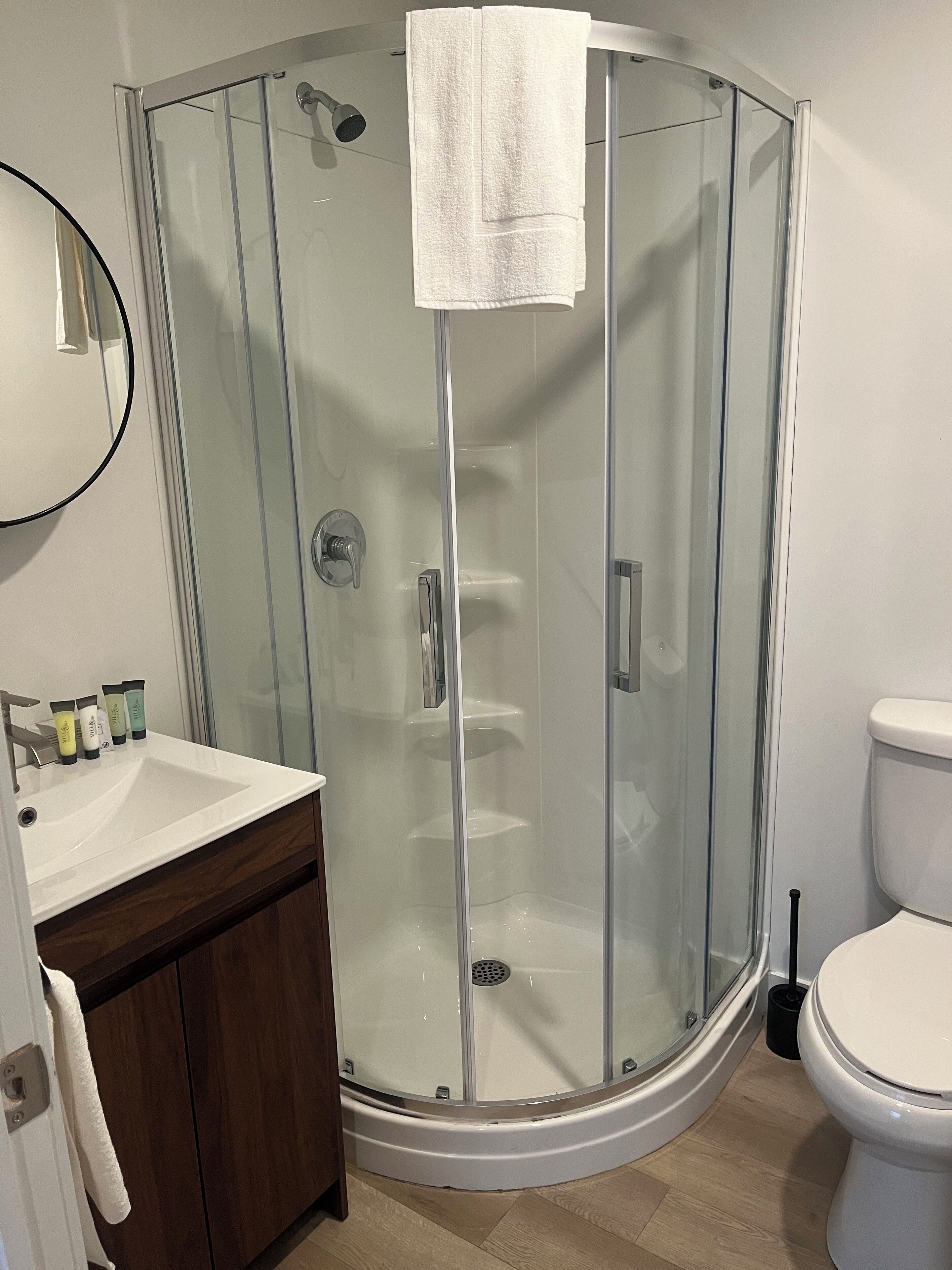 Une salle de bain avec une douche à parois de verre, un lavabo blanc, des toilettes et un miroir.