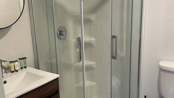 Une salle de bain avec une douche à parois de verre, un lavabo blanc, des toilettes et un miroir.