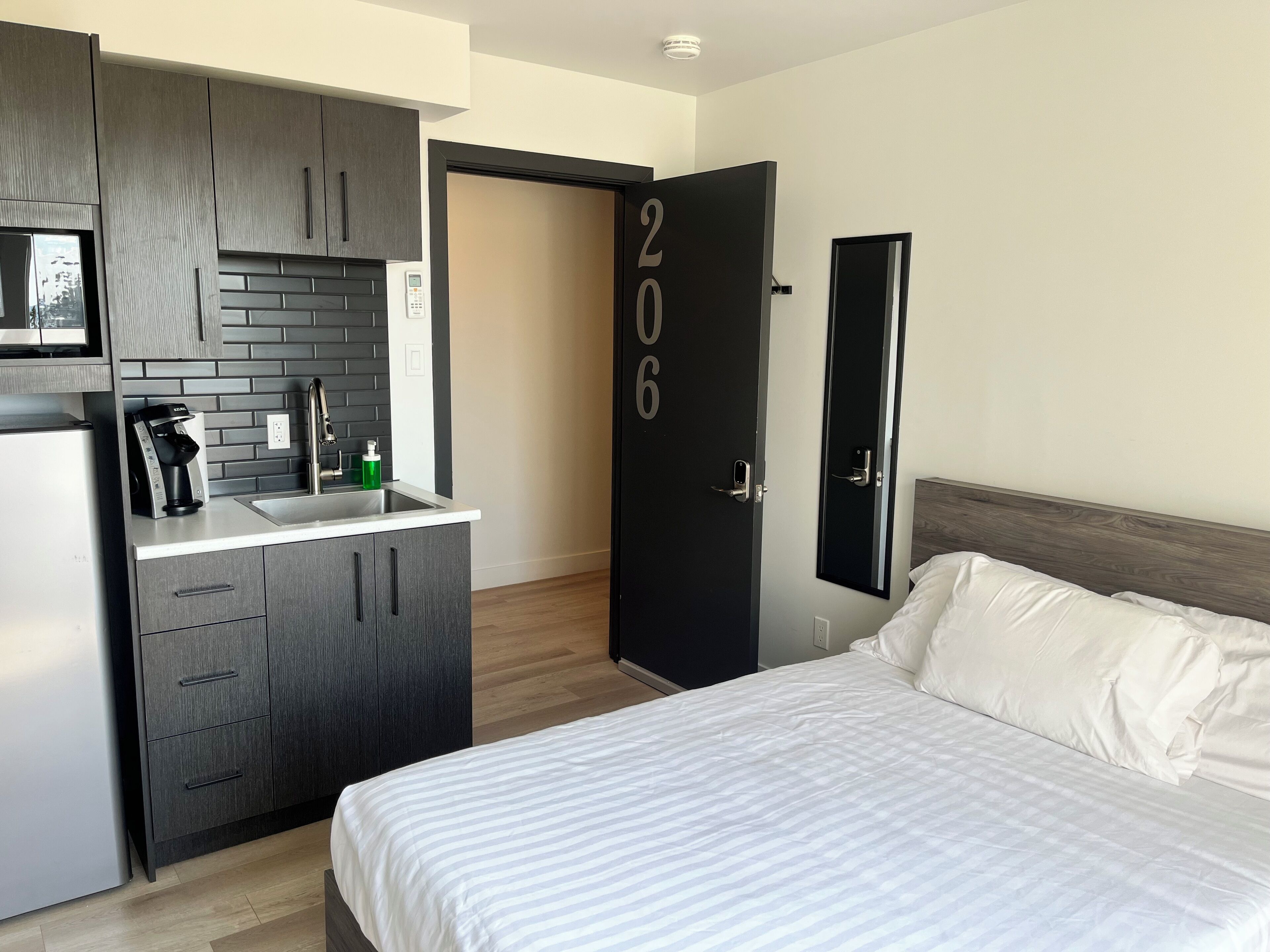 Une chambre d’hôtel de taille modeste, équipée d’une kitchenette, d’un lit et d’une porte portant le numéro 206.