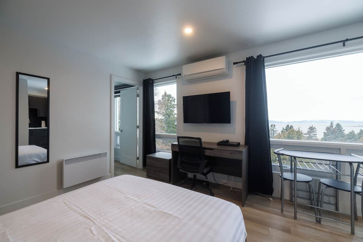 A bedroom with a bed, a desk, a chair, a TV, and a balcony with a table and chairs.