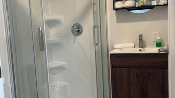 Een badkamer met een douchecabine van glas, een toilet, een wastafel met spiegel en een plank met toiletartikelen.