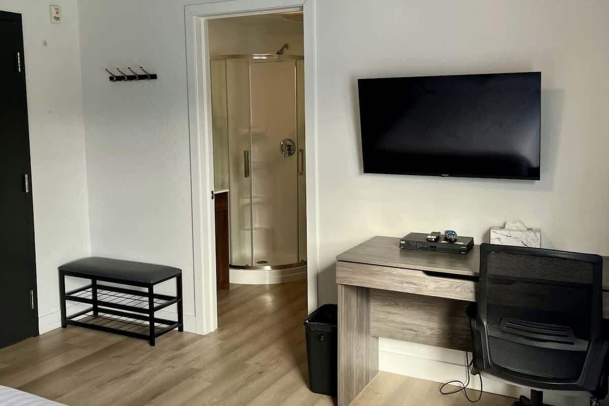 A hotel room with a bed, desk, chair, TV, and a shower area.