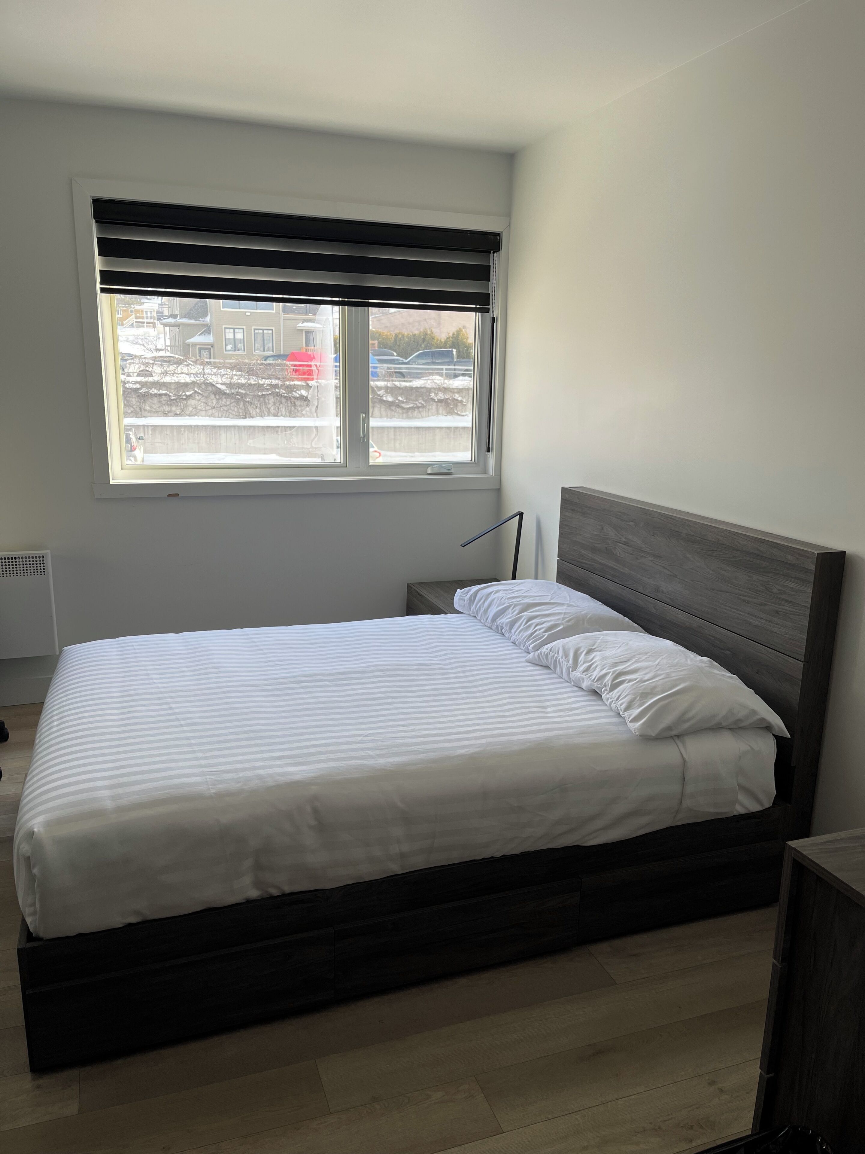 Une chambre à coucher avec un lit, une fenêtre avec des stores, un radiateur et une vue sur un espace extérieur enneigé.