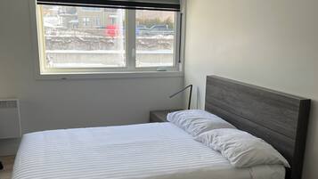 Une chambre à coucher avec un lit, une fenêtre avec des stores, un radiateur et une vue sur un espace extérieur enneigé.