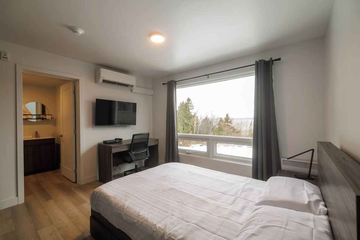 A bedroom with a bed, a desk, a television, and a window with curtains.