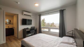 A bedroom with a bed, a desk, a television, and a window with curtains.