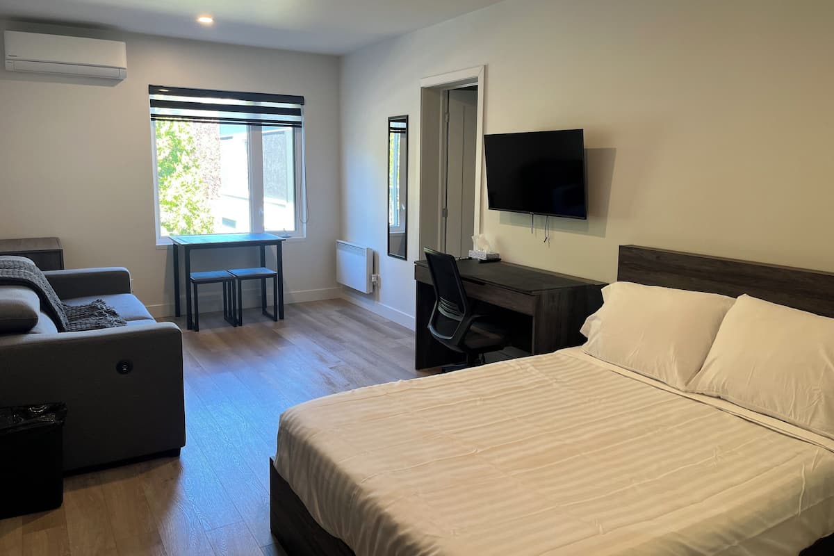 A hotel room with a bed, a desk, a chair, a TV, and a window.