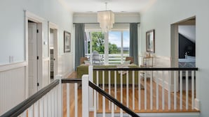 A spacious hallway with a staircase leading to a balcony. - OBX Rays: Stunning Soundfront Home, Private Heated Pool, Hot Tub, Community Amenities (Corolla)