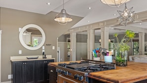 A modern kitchen with a central island, dark cabinetry, and a large stove. - OBX Rays: Stunning Soundfront Home, Private Heated Pool, Hot Tub, Community Amenities (Corolla)