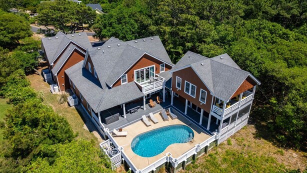 A large house with a swimming pool, multiple decks, and a view of the surrounding forest. - OBX Rays: Stunning Soundfront Home, Private Heated Pool, Hot Tub, Community Amenities (Corolla)