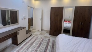 A bedroom with a bed, a wardrobe, a mirror, a desk, and a door leading to another room. - Spacious 2-Bedroom Apartment (Hurghada)