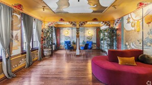 Ein geräumiges Zimmer mit Holzboden, einem roten Sofa und einer Chandelier. In der Mitte befinden sich zwei blaue Stühle und ein Tisch.